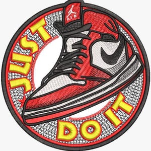 Peut inclure: Un écusson brodé circulaire représentant une basket montante rouge, blanche et noire. Le texte JUST DO IT est brodé en lettres capitales jaunes autour de la basket. Un petit logo Jumpman rouge et le mot AIR sont visibles en haut.