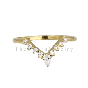 May include: A gold V-shaped ring featuring a central pear-cut clear stone flanked by five round-cut clear stones on each side. The band has a smooth polished finish. The text TheGaxiaJewelry is visible across the centre of the ring.