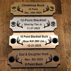 May include: Four metal plaques with engraved text and deer antler graphics. The plaques include details such as "Christmas Buck," "12-Point Blacktail," "10 Point Blacktail Buck," and "Dad & Daughter Hunt," along with dates and point counts.