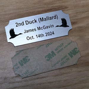 May include: A silver metal nameplate with rounded edges, featuring the text "2nd Duck (Mallard)", "James McGavin", and "Oct. 14th 2024". Two black duck silhouettes are on the plate. A 3M adhesive backing is below.
