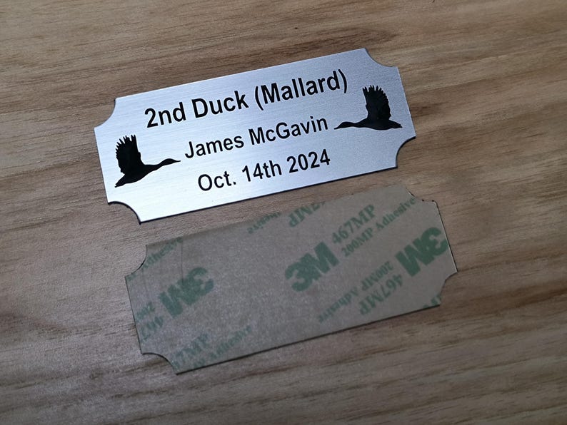 May include: A silver metal nameplate with rounded edges, featuring the text "2nd Duck (Mallard)", "James McGavin", and "Oct. 14th 2024". Two black duck silhouettes are on the plate. A 3M adhesive backing is below.