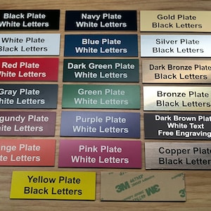 May include: A collection of rectangular nameplates in various colors including black, navy, gold, white, blue, silver, red, dark green, dark bronze, gray, green, bronze, burgundy, purple, dark brown, orange, pink, copper, and yellow with text.