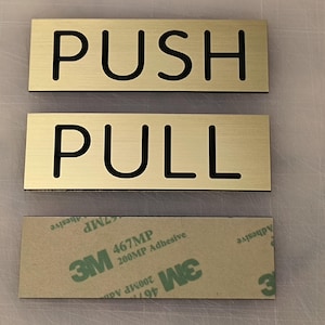 May include: Two gold-colored metal signs with black lettering. The top sign reads "PUSH" and the bottom sign reads "PULL".