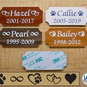 May include: Four wooden pet memorial plaques with different wood finishes and engraved text. The plaques feature a heart, paw print, and infinity symbol. The text on the plaques reads "Hazel 2001-2017", "Callie 2005-2019", "Pearl 1995-2009", and "Bailey 1998-2012".
