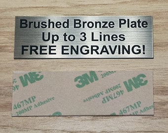 May include: A brushed bronze plate with the text "Brushed Bronze Plate Up to 3 Lines FREE ENGRAVING!" The plate has a silver finish and is attached to a sheet of adhesive backing.