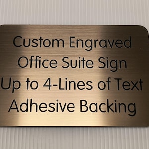 May include: A gold-colored metal sign with the text "Custom Engraved Office Suite Sign Up to 4-Lines of Text Adhesive Backing".