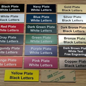May include: A collection of rectangular nameplates in various colors including black, navy, gold, white, blue, silver, red, dark green, dark bronze, gray, green, bronze, burgundy, purple, dark brown, orange, pink, copper, and yellow with text.