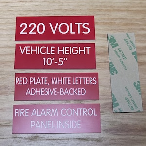 May include: Four red rectangular signs with white text. The top sign reads "220 VOLTS". The second sign reads "VEHICLE HEIGHT 10'-5" ". The third sign reads "RED PLATE, WHITE LETTERS ADHESIVE-BACKED". The bottom sign reads "FIRE ALARM CONTROL PANEL INSIDE".