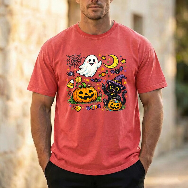 May include: A red short-sleeve t-shirt featuring a colorful Halloween graphic print. The design includes a white ghost, a large orange jack-o'-lantern, a black cat wearing a purple witch hat, a yellow crescent moon, stars, and candy.