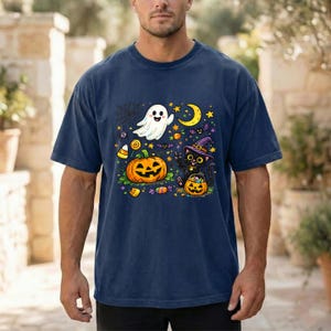 May include: A navy blue short-sleeve t-shirt featuring a colorful Halloween graphic. The design includes a white ghost, a large orange jack-o'-lantern, a black cat wearing a purple witch hat, a yellow crescent moon, stars, and candy.