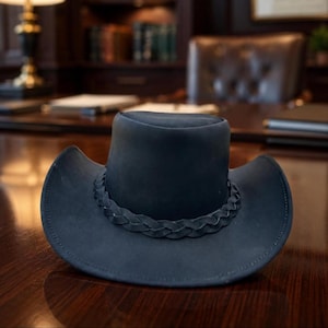 May include: A dark navy blue cowboy hat with a matte finish and a wide, curved brim. The hat features a decorative braided band encircling the base of the crown, matching the deep blue color of the hat's exterior surface and structured design.