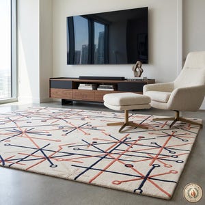 May include: A cream-colored area rug with a geometric pattern in navy blue and coral. The rug is in a modern living room setting, with a chair, ottoman, and entertainment center visible in the background.