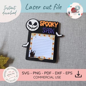 Op de afbeelding: Een zwarte lasergesneden notitieblokhouder met een wit schedelgezicht, twee witte vleermuizen en de oranje en paarse tekst "SPOOKY SEASON". Een rechthoekig notitieblok met gelinieerd papier, een spookhuisafbeelding en een pompoenrand.