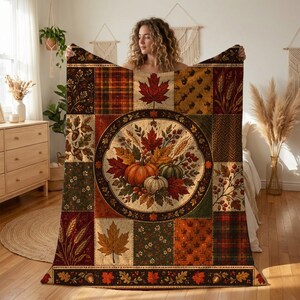 May include: A rectangular throw blanket featuring a patchwork design with autumn-themed patterns including maple leaves, pumpkins, acorns, wheat stalks, and plaid prints. The center displays a circular medallion with a harvest arrangement.