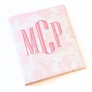 May include: A white fabric album with a pink toile pattern and the monogram "MCP" embroidered in pink.