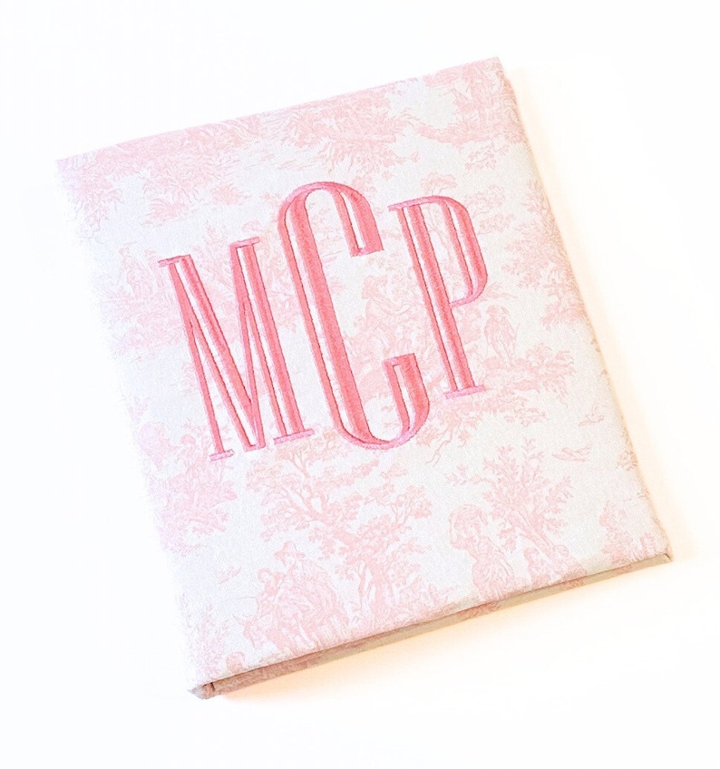 May include: A white fabric album with a pink toile pattern and the monogram "MCP" embroidered in pink.