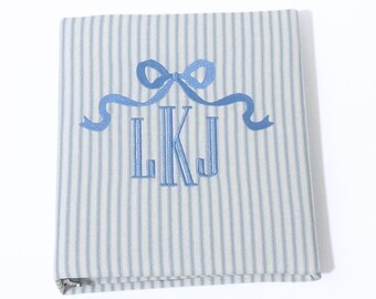May include: A blue and white striped fabric photo album with a blue ribbon and bow and the monogram LKJ embroidered on the front.