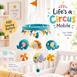 May include: A felt circus-themed mobile featuring a teal circular frame, hanging felt elephants in blue, yellow, and gray, and colorful striped balls. The mobile includes a bunting banner and an orange flag. Text reads Life's a Circus Mobile.