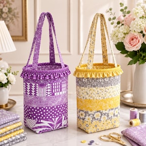 Könnte beinhalten: Zwei zylindrische Stofftaschen mit gerüschten oberen Rändern und zwei Tragegriffen. Eine Tasche zeigt violette Patchwork-Muster mit geometrischen Formen, Punkten und Blumen. Die andere Tasche hat gelbe und graue Blumen- und Spitzenmuster.