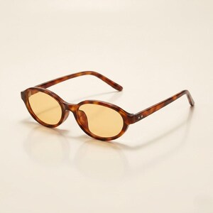 Peut inclure: Lunettes de soleil ovales avec une monture à motif écaille de tortue et des verres teintés jaunes. Les lunettes ont un design classique avec une forme subtile et arrondie. La monture est de couleur marron chaud avec des accents marron plus foncés.