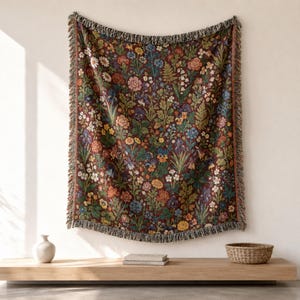 May include: A woven throw blanket featuring a dense, intricate botanical pattern of various flowers and foliage in shades of deep red, blue, yellow, and green against a dark background, finished with a decorative fringed edge on all sides.