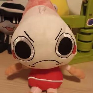 Peut inclure: Une peluche avec une grande t&ecirc;te blanche &agrave; l'expression f&acirc;ch&eacute;e, des yeux noirs circulaires et une petite bouche fronc&eacute;e. Le corps est rouge avec une bande horizontale blanche, et le sommet de la t&ecirc;te pr&eacute;sente une nageoire caudale ros&eacute;e.