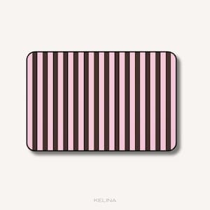 Peut inclure: Un tapis rectangulaire présentant un motif de rayures verticales répétitives dans des tons alternés de rose clair et de brun foncé. Le tapis a des coins arrondis et une fine bordure noire soulignant tout le périmètre. Le mot KELINA est imprimé en dessous.