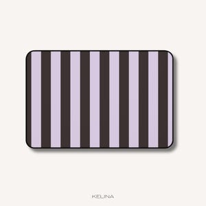 Peut inclure: Un tapis rectangulaire présentant un motif à rayures verticales alternant des nuances de lavande clair et de gris anthracite foncé. Le tapis a des coins arrondis et une fine bordure noire. Le mot KELINA est imprimé en petites lettres en dessous.