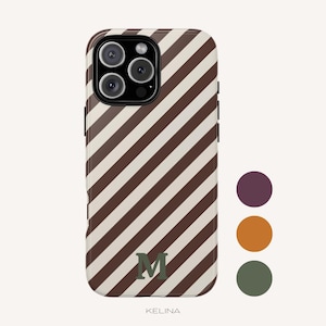 Op de afbeelding: Een smartphonehoesje met een diagonaal streeppatroon in donkerbruin en crème. Het hoesje heeft een gecentreerde donkergroene letter M aan de onderkant en een zwarte uitsparing voor de cameramodule. Rechts staan drie cirkelvormige kleurstaaltjes in paars, oranje en groen.