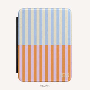 Op de afbeelding: Een rechthoekige hoes voor een e-reader met een verticaal streeppatroon. De bovenste helft toont lichtblauwe en crèmekleurige strepen, terwijl de onderste helft oranje en lavendelkleurige strepen heeft. De initialen KM staan rechtsonder afgedrukt.