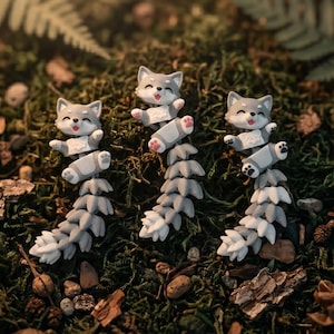 May include: Three articulated gray and white fox figurines with smiling expressions, open mouths, and long, segmented tails. Each fox features small pink paw pads on its feet and a detailed, flexible body structure designed for movement.