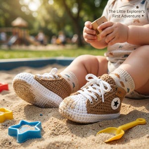 Puede incluir: Zapatillas de bebé de ganchillo en marrón y blanco, con cordones blancos y un emblema de estrella negra. Los zapatos son de la talla 1.1 y están en una caja de arena con un juguete en forma de estrella azul y una pala amarilla.