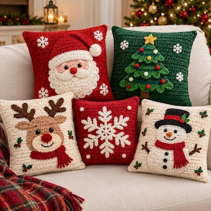 Può includere: Cinque cuscini quadrati all'uncinetto con motivi natalizi: un Babbo Natale rosso, un albero di Natale verde, una renna color crema con naso rosso, un fiocco di neve rosso e un pupazzo di neve color crema con cappello nero e sciarpa rossa.