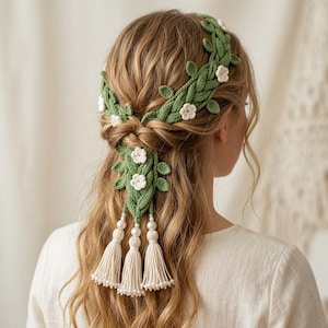 May include: A green crocheted headband featuring leaves and white flowers, worn in the hair. The design includes tassels and beads, giving a bohemian look. The hair is long and wavy, with a braid at the back.
