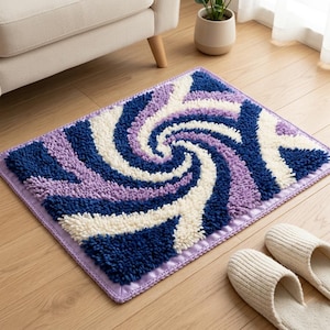 May include: A rectangular bath mat with a spiral design in shades of blue, purple, and white. The mat has a soft, textured surface and a lavender border. Two white slippers are next to the mat.