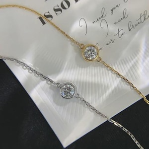 Puede incluir: Dos pulseras delicadas, una en metal dorado y otra en metal plateado, cada una con una piedra redonda, clara y facetada engastada en un bisel en el centro de un diseño de cadena fina y delgada.