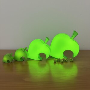 Op de afbeelding: Een verzameling gloeiende groene bladvormige decoraties, waaronder grote en kleine bladeren. De items zijn gerangschikt op een houten oppervlak, met een zachte groene gloed die ervan uitgaat.