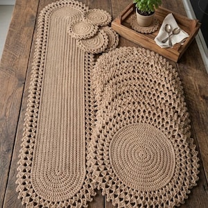 Peut inclure: Un ensemble de linge de table en crochet beige comprenant un long chemin de table, plusieurs sets de table ronds et de petits dessous de verre circulaires. Chaque pièce présente un centre dense et texturé avec une bordure festonnée ajourée.