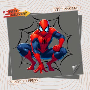 May include: A DTF transfer featuring a graphic illustration of a superhero in a red and blue suit with a black spider emblem on the chest, crouching in front of a black spiderweb design. The image includes the text FAST DELIVERY and READY TO PRESS.