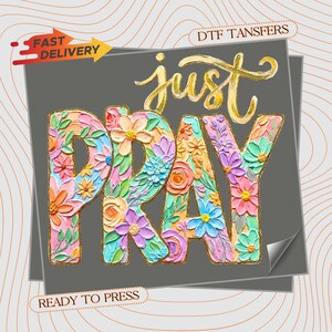 May include: A DTF transfer sheet featuring the gold text 'just' above the word 'PRAY' in large, block letters. The letters are filled with a colorful, textured floral pattern in shades of pink, blue, orange, and green. Includes 'FAST DELIVERY' and 'READY TO PRESS' text.