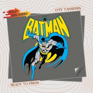 May include: A DTF transfer sheet featuring a graphic of Batman in a dynamic pose with a blue cape, yellow utility belt, and grey suit. The word BATMAN appears in large yellow letters above the character. Text includes FAST DELIVERY and READY TO PRESS.
