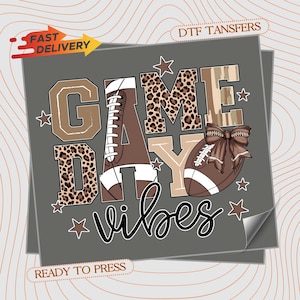 May include: A gray graphic with the words "GAME DAY vibes" in a mix of fonts and patterns. The design includes footballs, stars, and leopard print accents. The words "Fast Delivery" and "Ready to Press" are also visible.