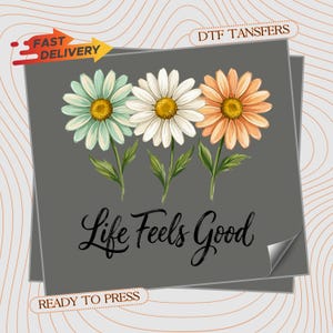 May include: A gray DTF transfer sheet featuring three daisy-like flowers in light blue, white, and peach with yellow centers. Below the flowers, the black cursive text reads Life Feels Good. The sheet includes text labels for Fast Delivery and Ready to Press.