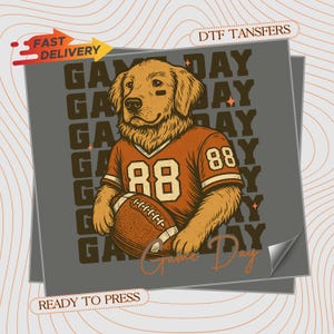 May include: A graphic transfer featuring a golden retriever wearing an orange football jersey with the number 88, holding a brown football. The background displays the repeated text GAME DAY in dark brown, with the script text Game Day below.