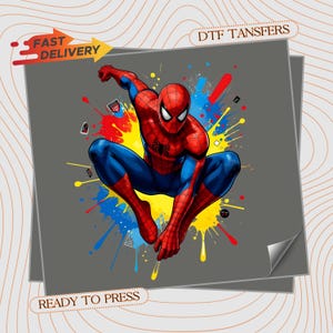 May include: A DTF transfer sheet featuring a graphic illustration of Spider-Man in a dynamic crouching pose. The character is rendered in red and blue with a black web pattern, set against a vibrant background of yellow, red, and blue paint splatters.