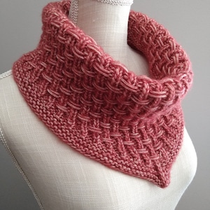 May include: A knitted cowl in a deep red color with a subtle white fleck throughout. The cowl is displayed on a white mannequin.