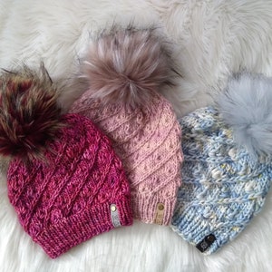 May include: Three knitted hats with faux fur pom-poms. The hats are in shades of pink, blue, and red.