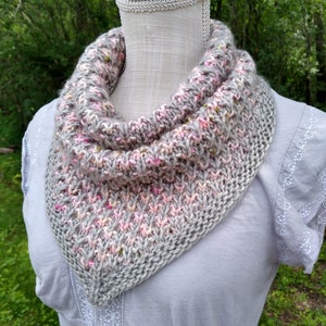 Può includere: Un collo a lupetto di maglia grigio, rosa e bianco con un motivo maculato. Il collo è drappeggiato su un manichino bianco.