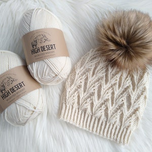 May include: Two skeins of white High Desert Worsted Weight yarn and a white knitted hat with a brown faux fur pom pom.