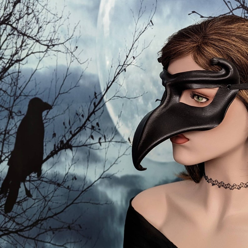 May include: A woman wearing a black leather masquerade mask with a long, curved beak. The mask covers her eyes and part of her face. She is wearing a black choker necklace and has long, brown hair.